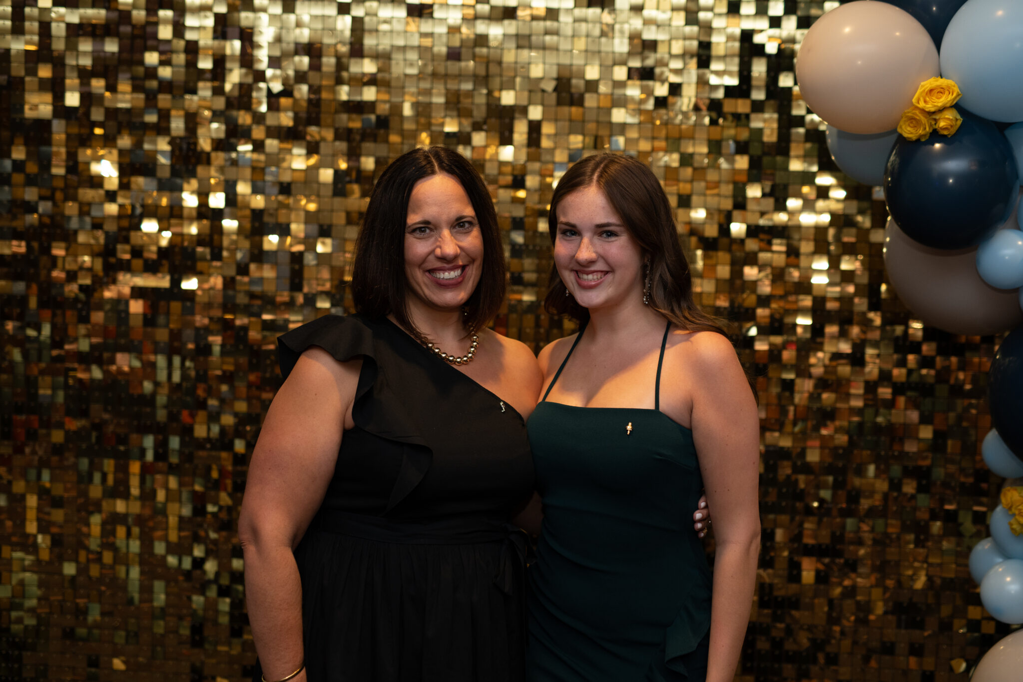 Two women smiling in front of a shimmer wall.